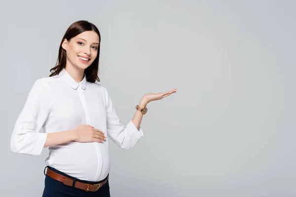 Souriant jeune femme d'affaires enceinte pointant de côté isolé sur gris — Photo de stock