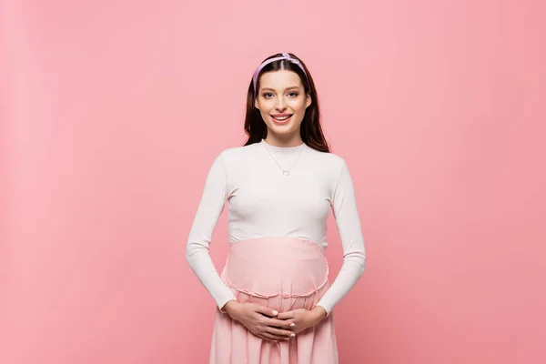 Heureux jeune jolie femme enceinte toucher ventre isolé sur rose — Photo de stock