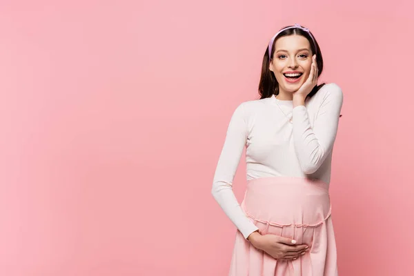 Щаслива молода красива вагітна жінка торкається живота ізольована на рожевому — стокове фото