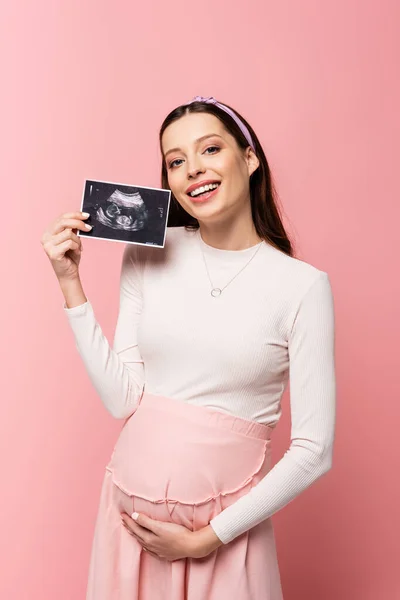 Happy young pretty pregnant woman holding ultrasound scan isolated on pink — Stock Photo