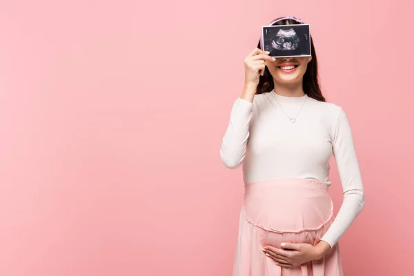 Glückliche junge hübsche schwangere Frau hält Ultraschalluntersuchung isoliert auf rosa — Stockfoto