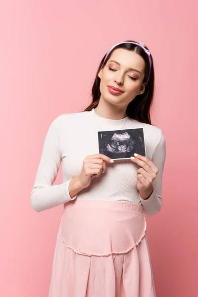 Joven bastante embarazada mujer sosteniendo ultrasonido escaneado aislado en rosa - foto de stock