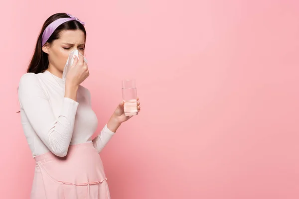 Young pretty pregnant woman with runny nose and water isolated on pink — Stock Photo