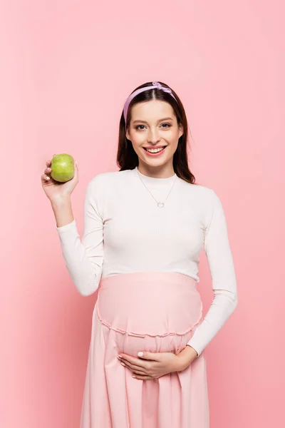 Счастливая молодая красивая беременная женщина с яблоком изолированы на розовый — стоковое фото