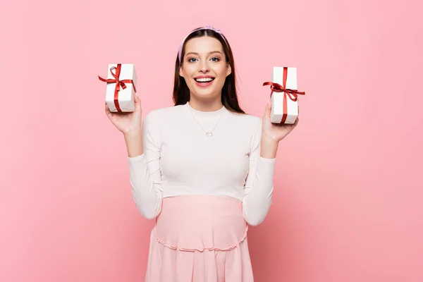 Feliz joven bastante embarazada mujer con regalos aislados en rosa - foto de stock
