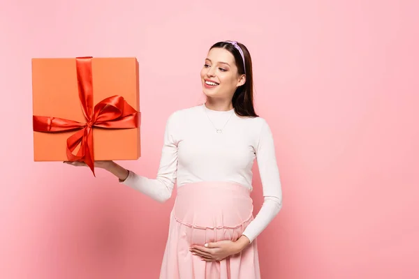 Happy young pretty pregnant woman with gift isolated on pink — Stock Photo