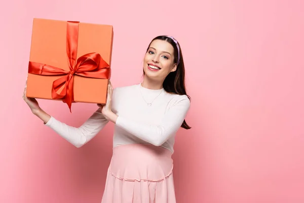 Счастливая молодая красивая беременная женщина с подарком изолированы на розовый — стоковое фото