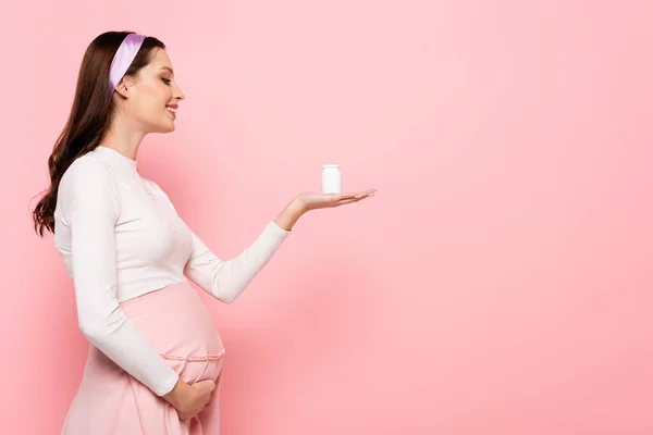 Feliz joven bastante embarazada mujer con vitaminas aisladas en rosa - foto de stock