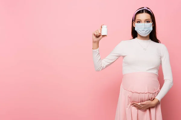 Jovem grávida em máscara médica com pílulas isoladas em rosa — Fotografia de Stock