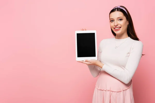 Feliz joven bonita mujer embarazada con tableta digital aislada en rosa - foto de stock