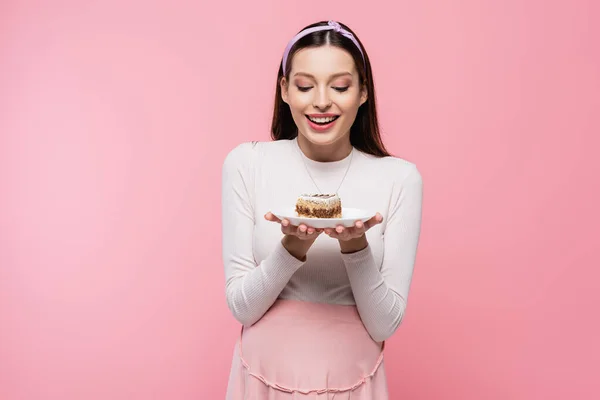 Happy young pretty pregnant woman with cake isolated on pink — Stock Photo