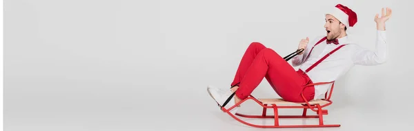 Excited man in santa hat sitting on sleigh on grey background , banner — Stock Photo