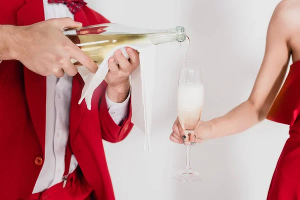 Cropped view of man in red suit pouring champagne in glass near woman on grey background — Stock Photo