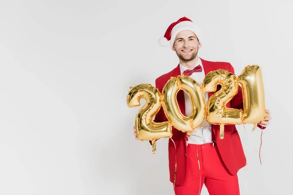 Smiling man in suit and santa hat holding balloons in shape of 2021 numbers on grey background — Stock Photo