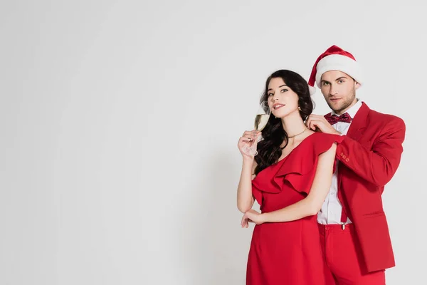 Mann mit Weihnachtsmütze und Anzug trägt Halskette auf brünette Frau mit Glas Champagner auf grauem Hintergrund — Stockfoto