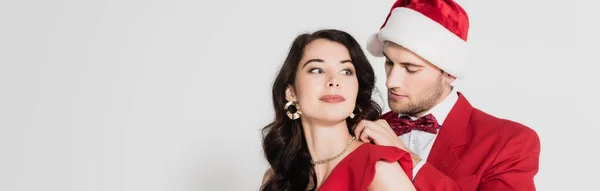 Young man in santa hat wearing necklace on brunette girlfriend on grey background, banner — Stock Photo
