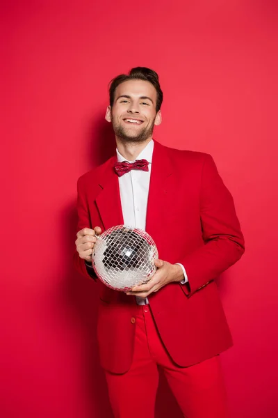 Homme souriant en costume rouge tenant boule disco sur fond rouge — Photo de stock