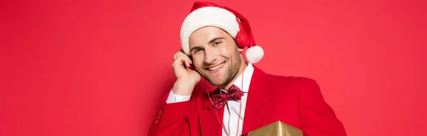 Hombre con estilo en sombrero de santa escuchar música en auriculares sobre fondo rojo, pancarta - foto de stock