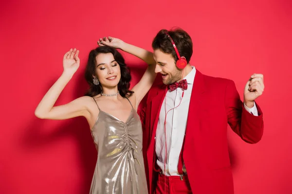 Hombre alegre en auriculares bailando cerca de novia sobre fondo rojo - foto de stock