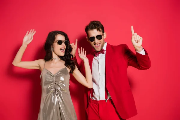 Couple élégant en lunettes de soleil dansant sur fond rouge — Photo de stock