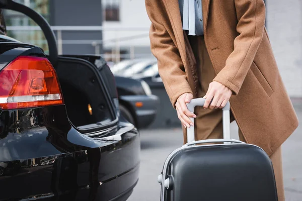 Vista parziale della donna in abiti autunnali con valigia vicino al bagagliaio dell'auto aperta — Foto stock