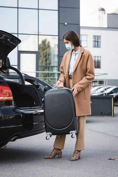Elegante donna in abito autunnale con valigia vicino al bagagliaio dell'auto — Foto stock