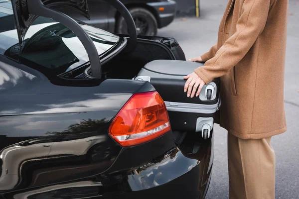 Vista recortada de la mujer en ropa de otoño poner maleta en el maletero del coche - foto de stock