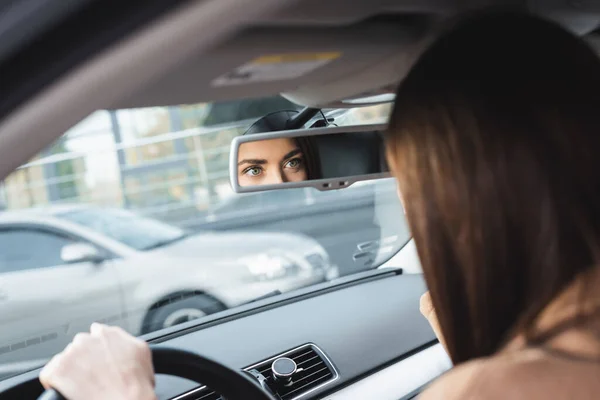 Женщина за рулем автомобиля и глядя в зеркало заднего вида на размытом переднем плане — стоковое фото