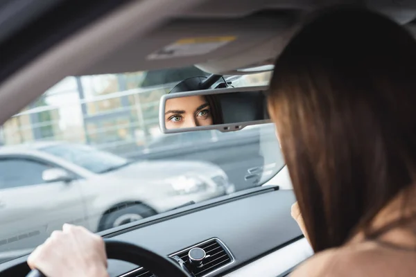 Frau fährt Auto und blickt in Rückspiegel auf verschwommenen Vordergrund — Stockfoto