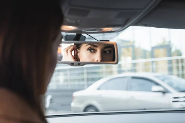 Donna che fissa i capelli guardando nello specchio retrovisore dell'auto in primo piano sfocato — Foto stock