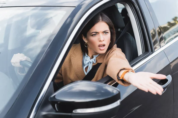 Irritated woman shouting and pointing with hand from side window while driving car on blurred foreground — Stock Photo