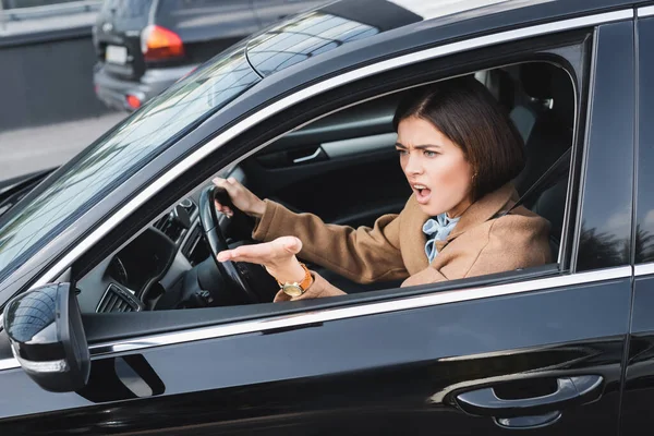 Angry woman screaming and pointing with hand from side window while driving car — Stock Photo