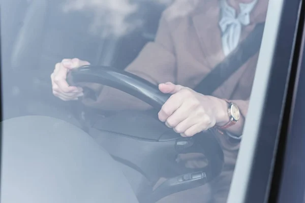 Vista recortada de la mujer sosteniendo el volante mientras conduce el coche en primer plano borroso - foto de stock