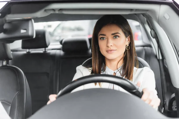 Femme souriante regardant vers l'avenir tout en conduisant la voiture sur le premier plan flou — Photo de stock