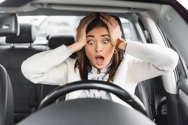 Mulher assustada de mãos dadas na cabeça enquanto sentado no carro e olhando para o volante — Fotografia de Stock