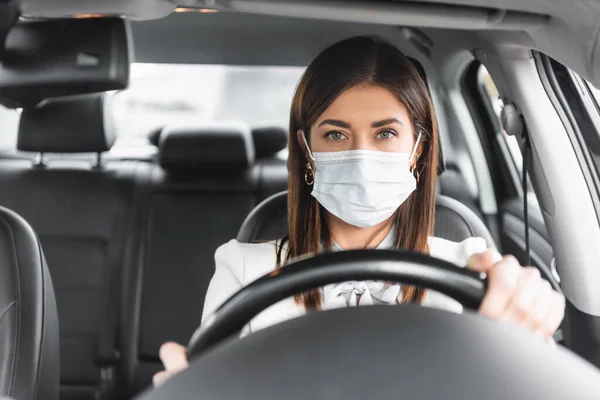 Frau in medizinischer Maske blickt während Autofahrt auf verschwommenen Vordergrund in die Kamera — Stockfoto