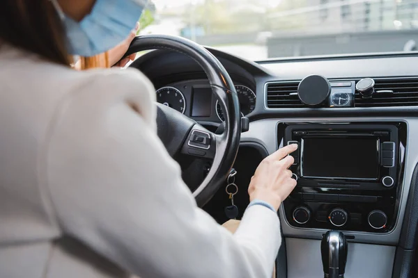 Cropped view of woman in medical mask pushing button on dashboard while sitting in car — Stock Photo