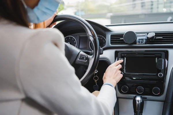 Vista recortada de la mujer en la máscara médica pulsando el botón en el tablero de instrumentos mientras está sentado en el coche - foto de stock