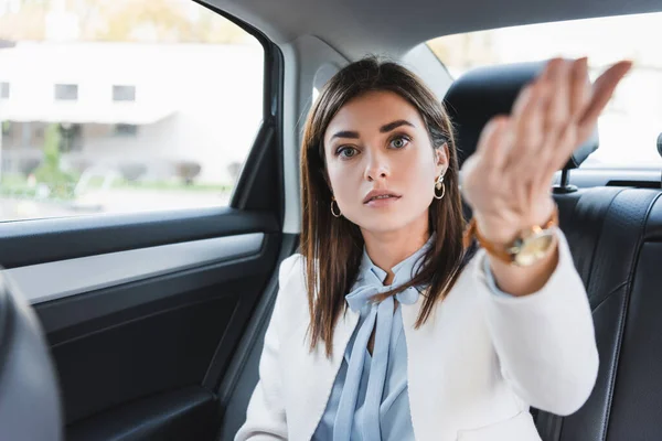 Femme élégante pointant avec la main tout en étant assis sur le siège arrière de la voiture sur le premier plan flou — Photo de stock