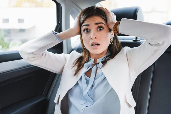 Frightened woman holding hands on head while sitting on back seat of car — Stock Photo