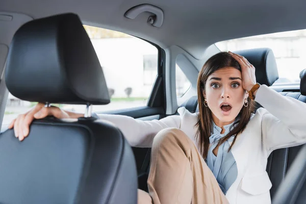 Scared woman holding hand on head while riding in car on blurred foreground — Stock Photo