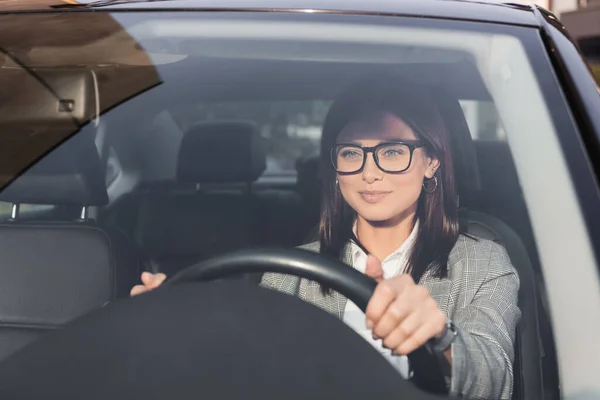 Smiling businesswoman looking ahead while driving car on blurred foreground — Stock Photo