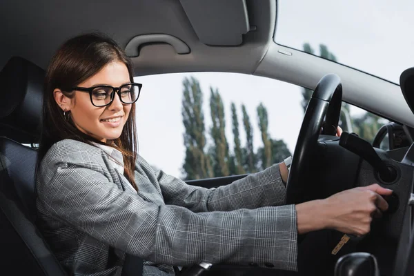 Mulher de negócios feliz em óculos sorrindo ao iniciar o carro — Fotografia de Stock