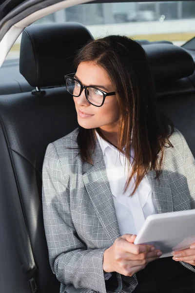 Улыбающаяся деловая женщина с цифровым планшетом смотрит в сторону во время езды в машине — стоковое фото