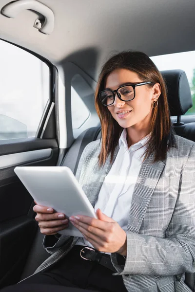 Позитивная деловая женщина, использующая цифровой планшет во время езды на автомобиле на заднем сидении — стоковое фото