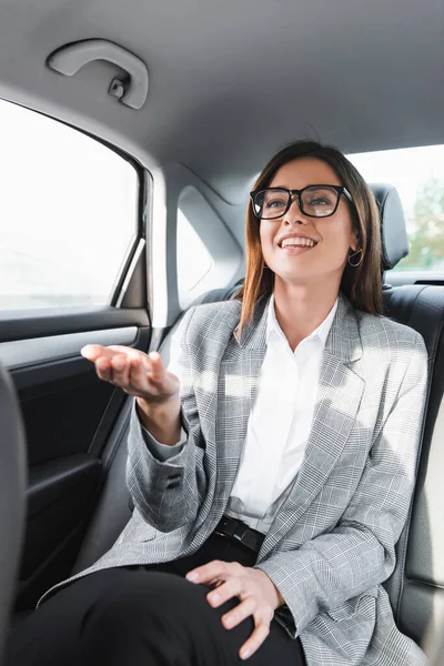 Веселая деловая женщина в очках, указывающая рукой, когда едет в машине — стоковое фото