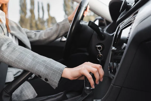 Cropped view of businesswoman shifting gear lever while driving car on blurred background — Stock Photo