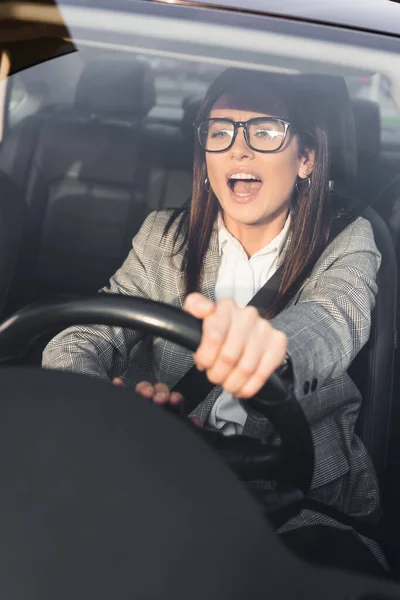 Femme en colère criant et bip tout en conduisant la voiture et regardant vers l'avant sur le premier plan flou — Photo de stock