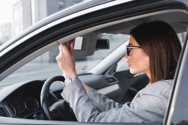 Mujer de negocios ajustando espejo retrovisor mientras está sentado en el coche - foto de stock