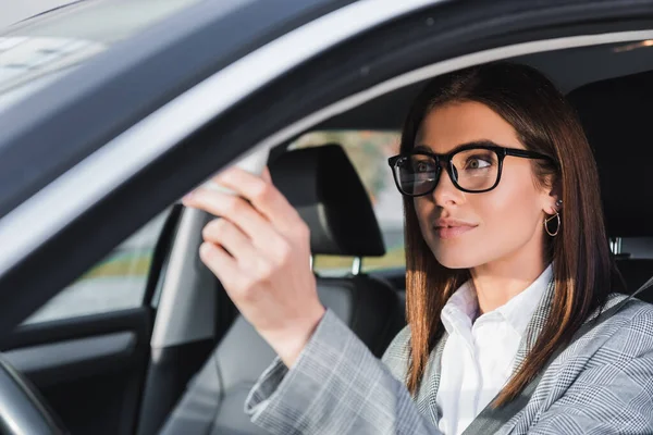 Elegante donna d'affari in occhiali seduta in auto in primo piano sfocato — Foto stock